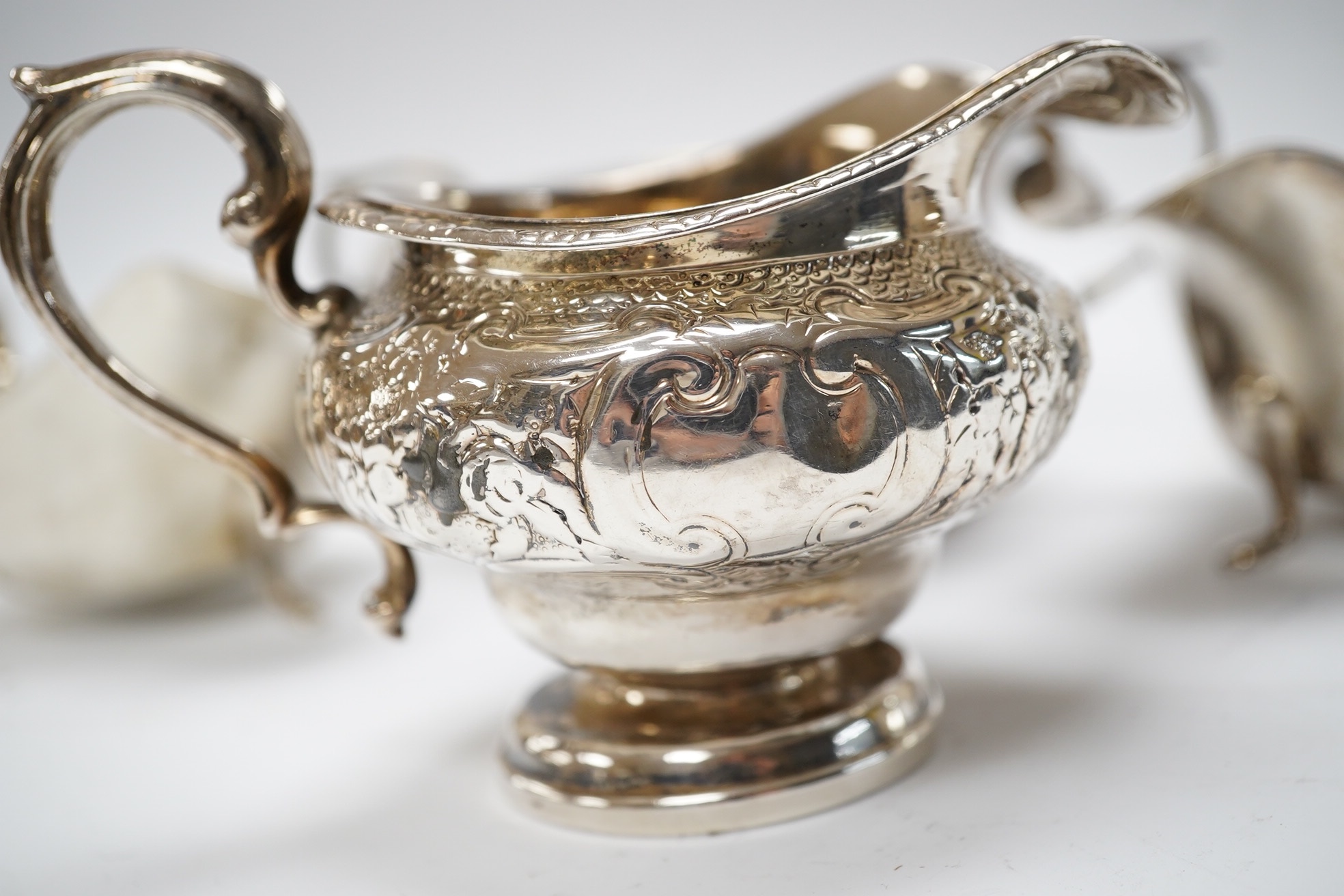 A George III Scottish silver cream jug, later embossed, a pair of George V silver sauce boats and an Edwardian hammered silver two handled porringer, by Moss Morris,18.4oz. Condition - poor to fair